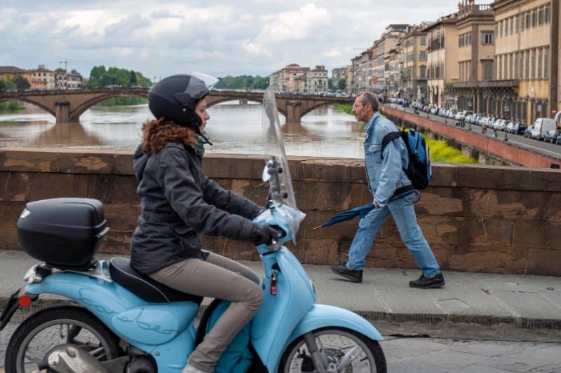 Woman riding Vespa across a bridge