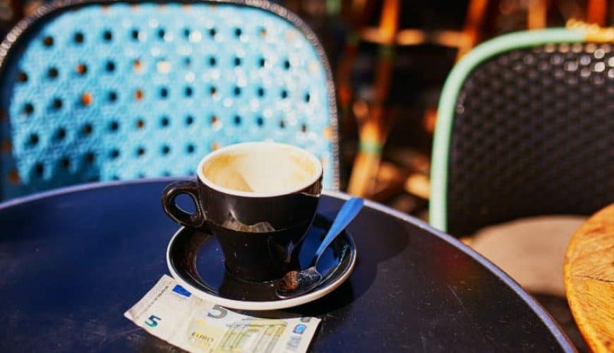 Empty cup of black coffee and 5 euro bank note on a table