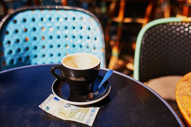 Empty cup of black coffee and 5 euro bank note on a table 