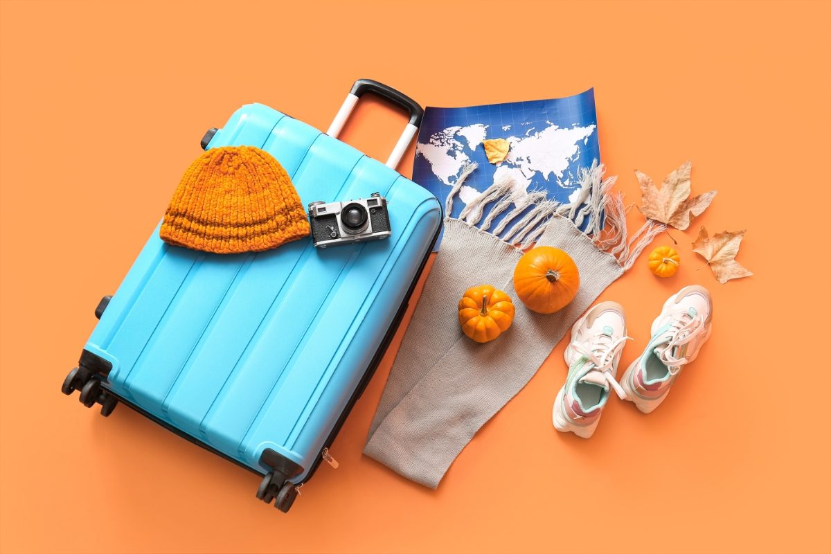 Top view of autumn travel essentials, including cozy fall outfits, a map, and a light blue suitcase