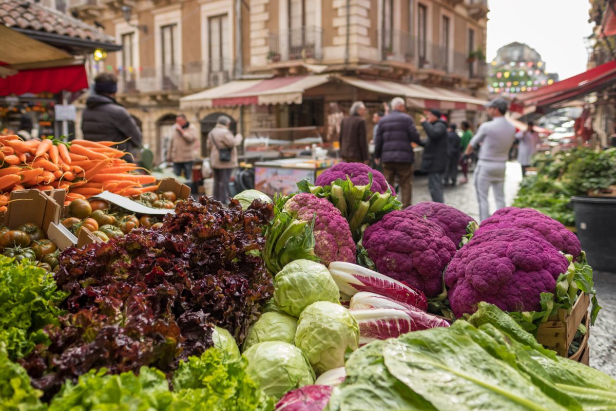 Vegetables, stalls, and people shopping at Ballarò Market in Palermo, Italy