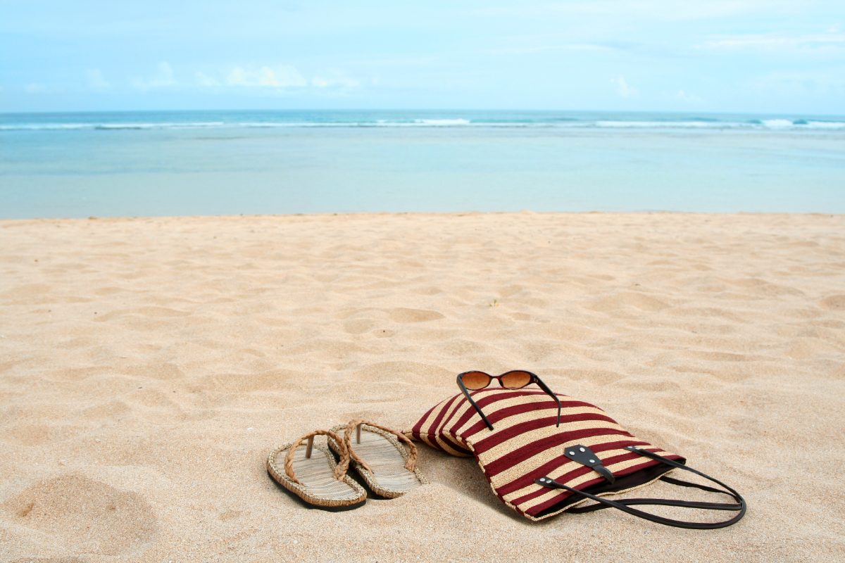 Beach sandals, a stylish bag, and sunglasses neatly arranged on the sand