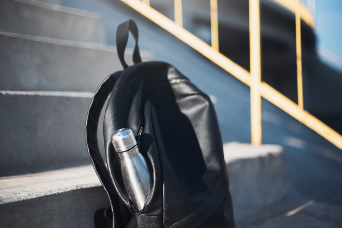 Close-up of a black backpack resting on stairs, with a reusable steel thermal water bottle neatly tucked into its side pocket