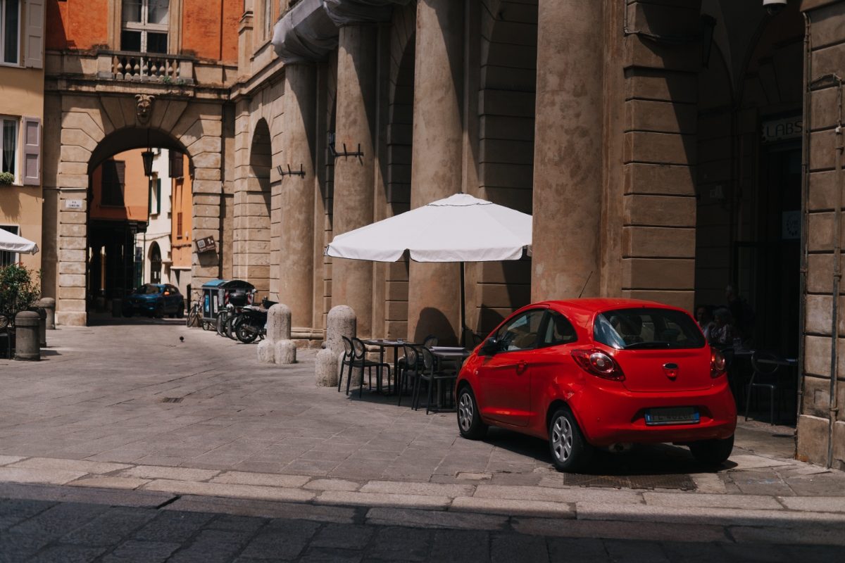 Red compact car parked on a street in Bologna, Italy