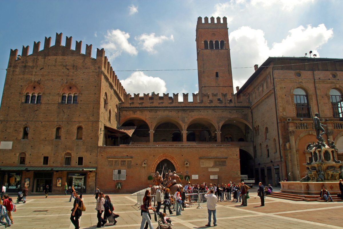 Tourists and locals walking and exploring in front of the Palazzo Re Enzo in Bologna, Italy