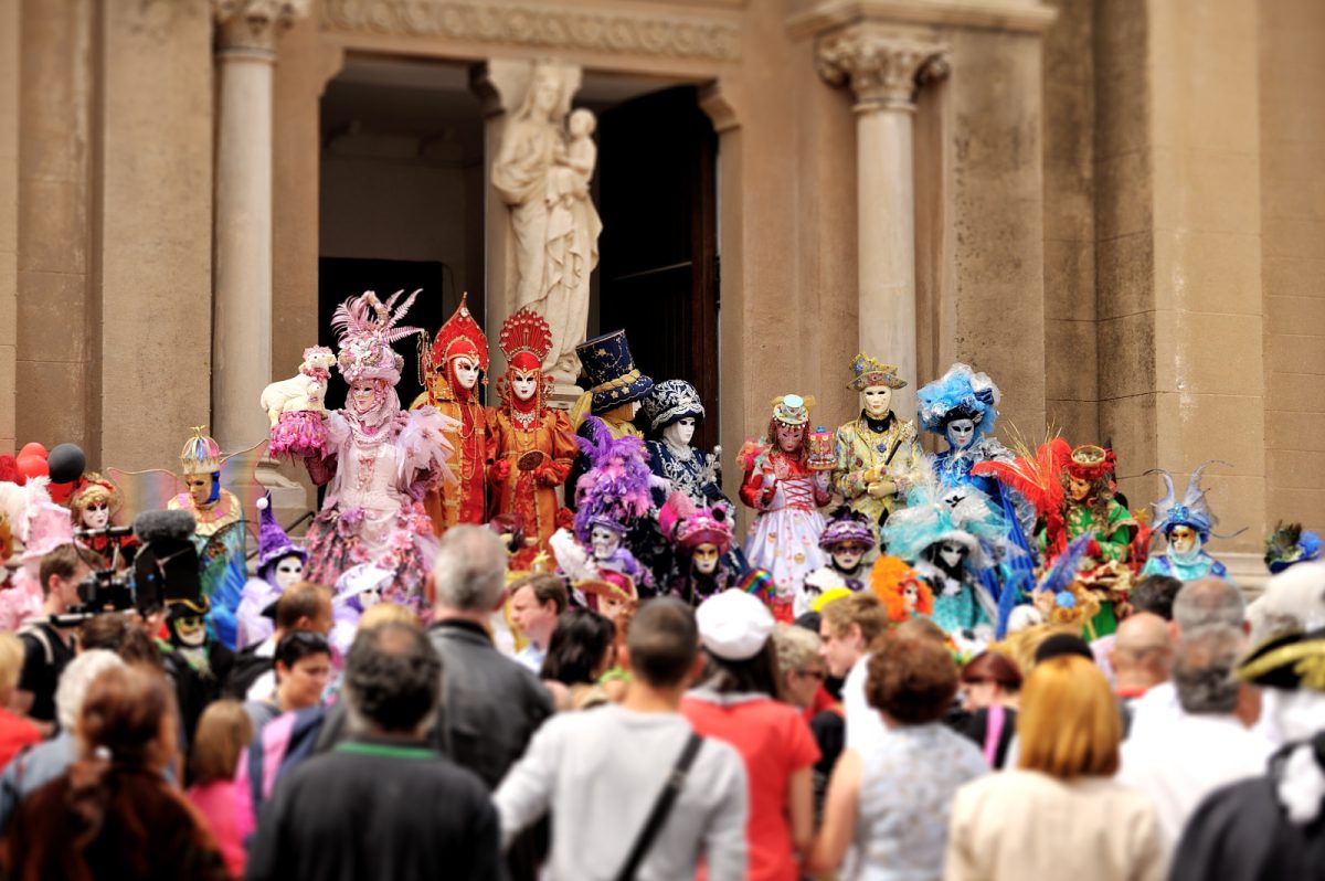 Tourists and locals are watching the Carnival of Venice parade, featuring people wearing colorful costumes and masks