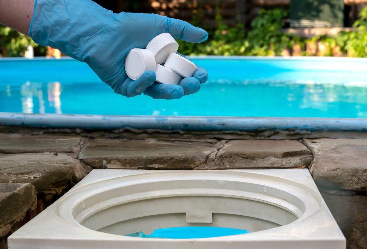 Hand putting 4 pieces of chlorine tablets  into the pool chlorinator