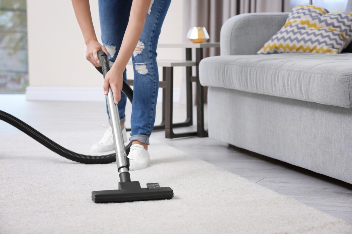 Woman in the living room cleaning a carpet with vacuum