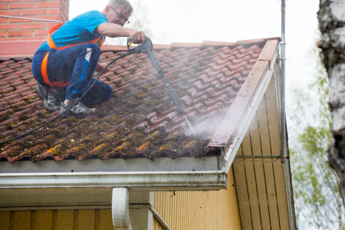 Man washing and cleaning a dirty roof with a high pressure washer