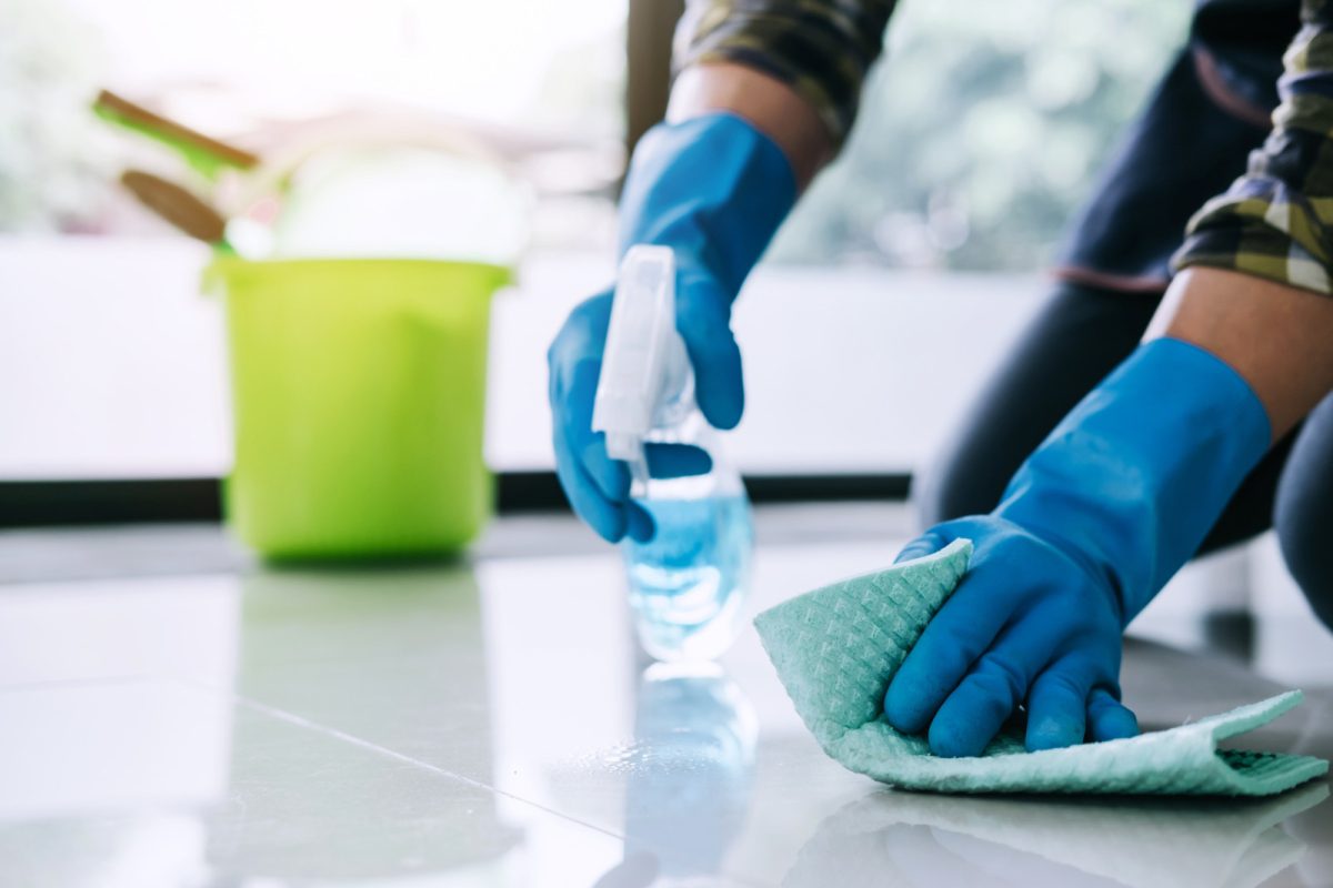 Man wearing a blue rubber gloves cleaning the floor with a wipe and a spray