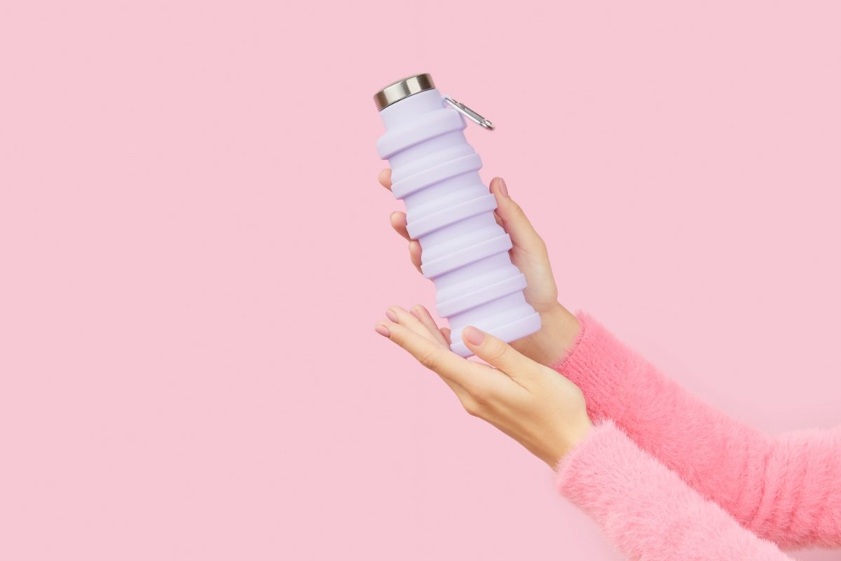 Hand holding a collapsible and reusable water bottle on pink background