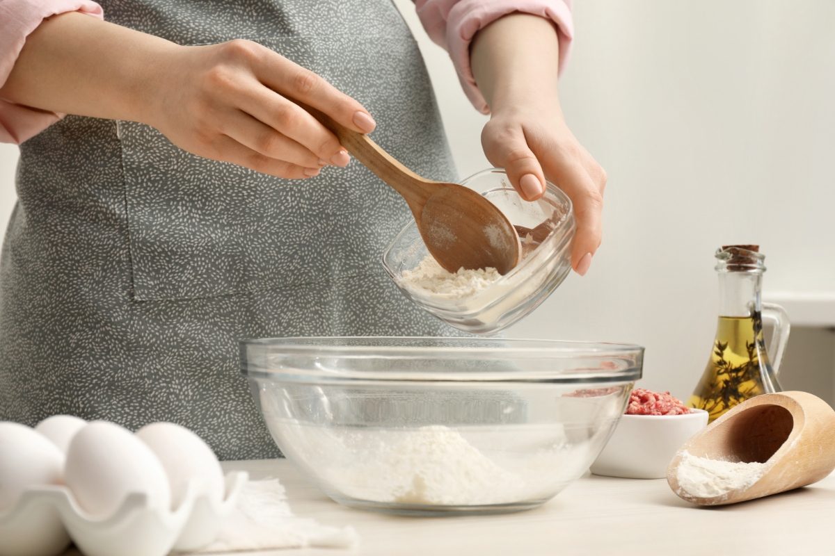 Woman preparing a meal putting flour into bowl for cooking