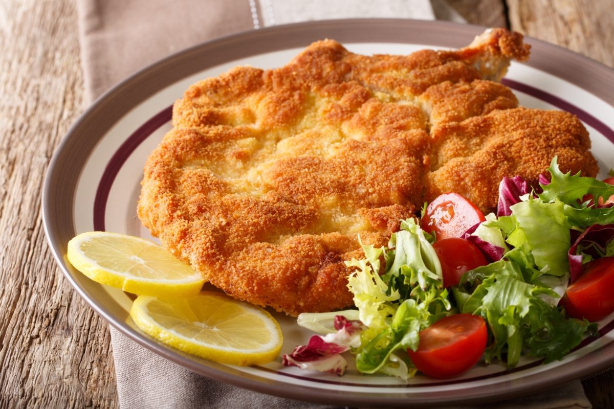 Close-up of the Cotoletta alla Milanese or the Veal Milanese with lemon and salad served on a plant