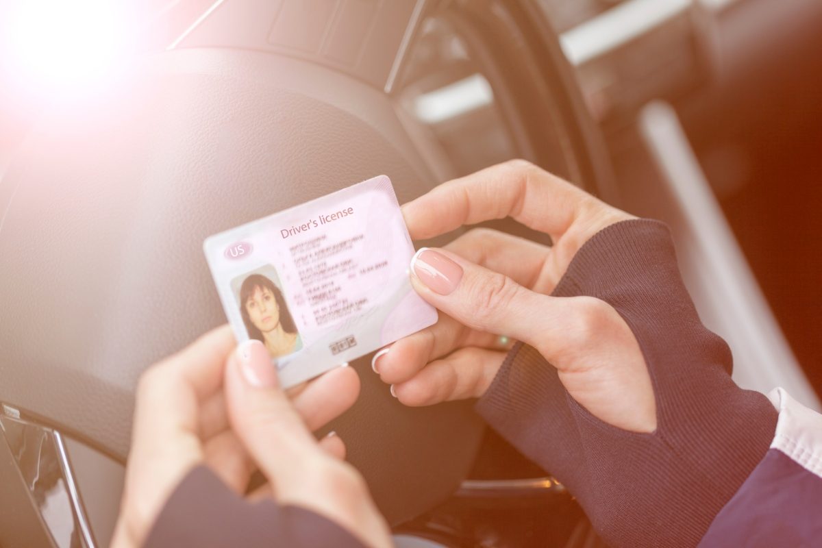 Woman holds a driver’s license while seated inside a car