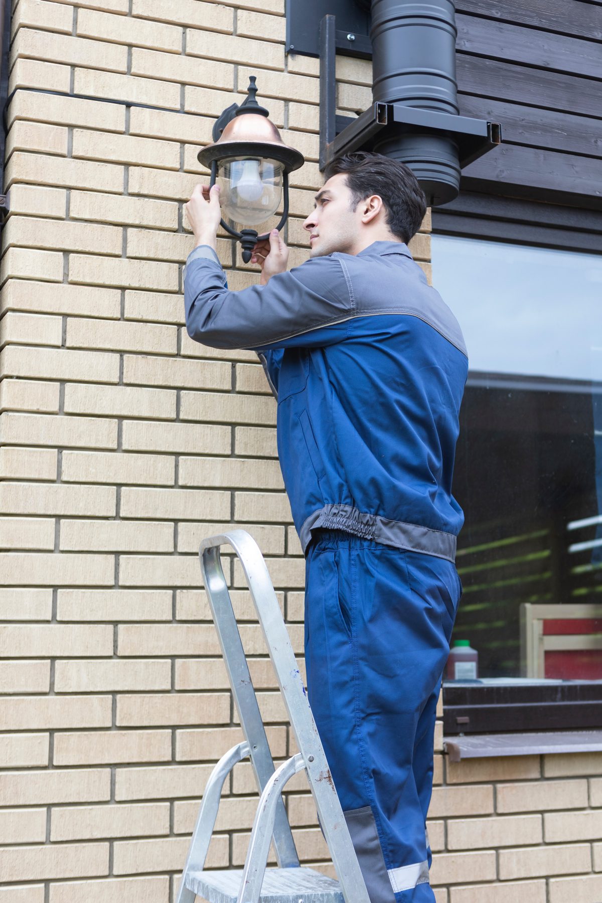 Electrician standing on ladder fixing and checking the outdoor lights