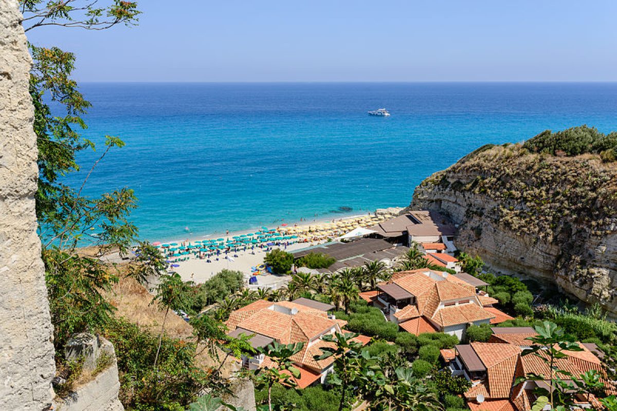 A breathtaking view of a tranquil beach in Italy, with soft golden sands meeting the clear turquoise waters of the Mediterranean Sea.