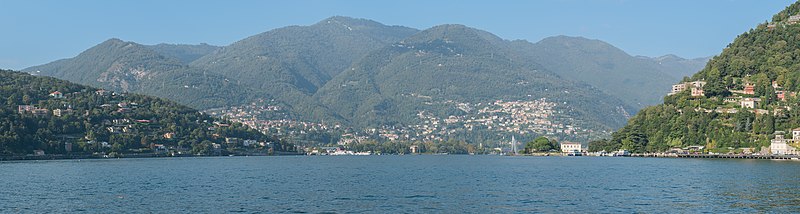 A breathtaking view of Lake Como in Italy, surrounded by lush green mountains, with colorful lakeside villas and boats floating on the tranquil waters.