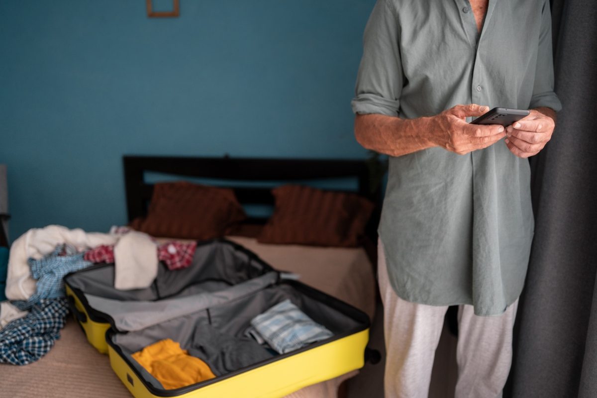 Man stands next to an open suitcase, packing clothes with focus and care