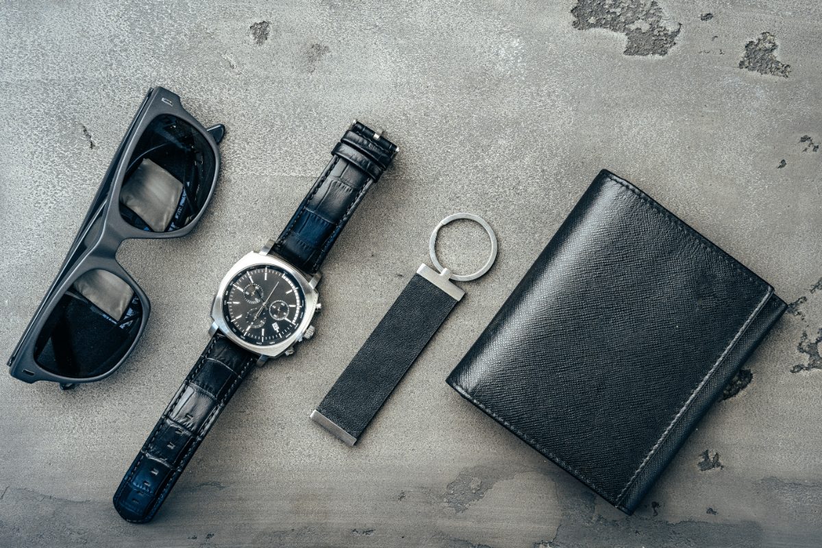 Close-up of male accessories including a sleek wallet, a stylish watch, and a pair of classic sunglasses