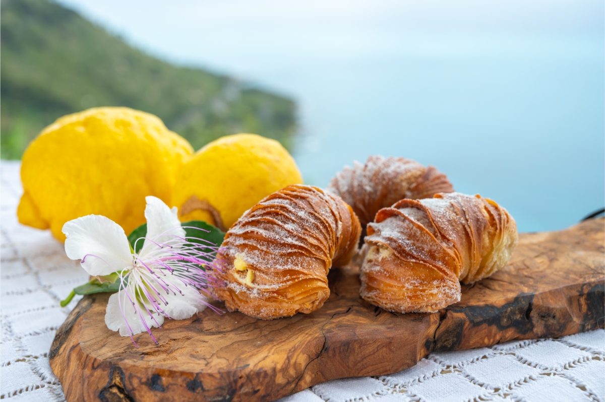 Naples shell-shaped pastry sfogliatella on a wood block next to a lemon and flower