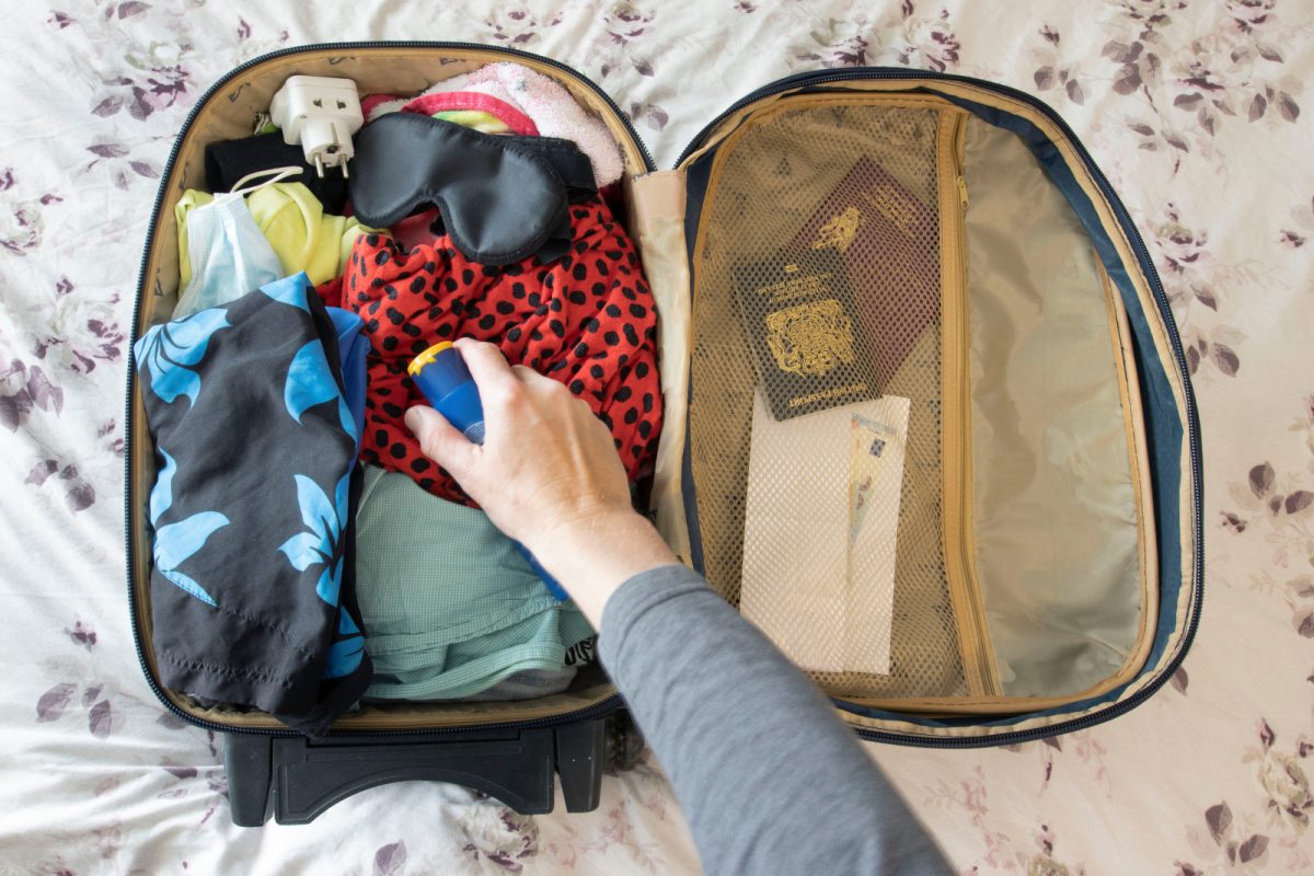 Packing a suitcase with clothes, passport, eye mask, and different travel essentials