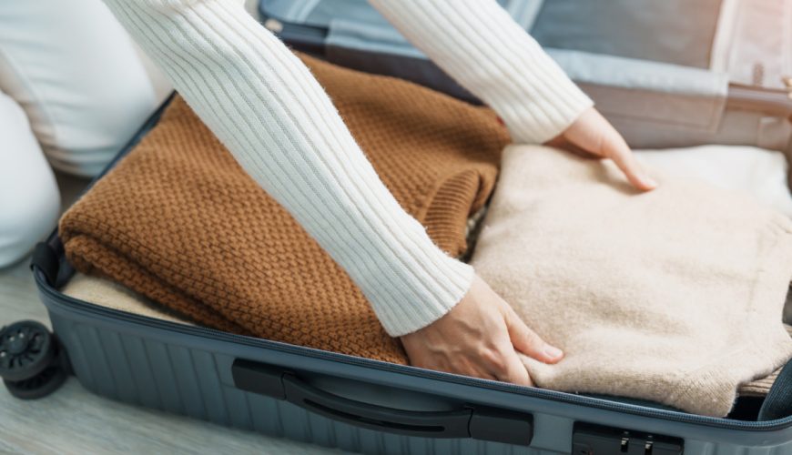 Woman packing winter clothes in luggage for travel preparation