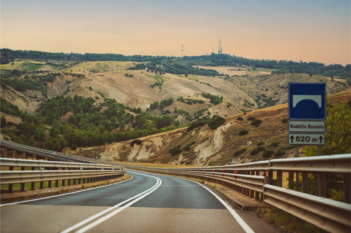 Scenic road trip in Puglia, Italy, featuring hills, mountains, and a sunset sky along an empty road