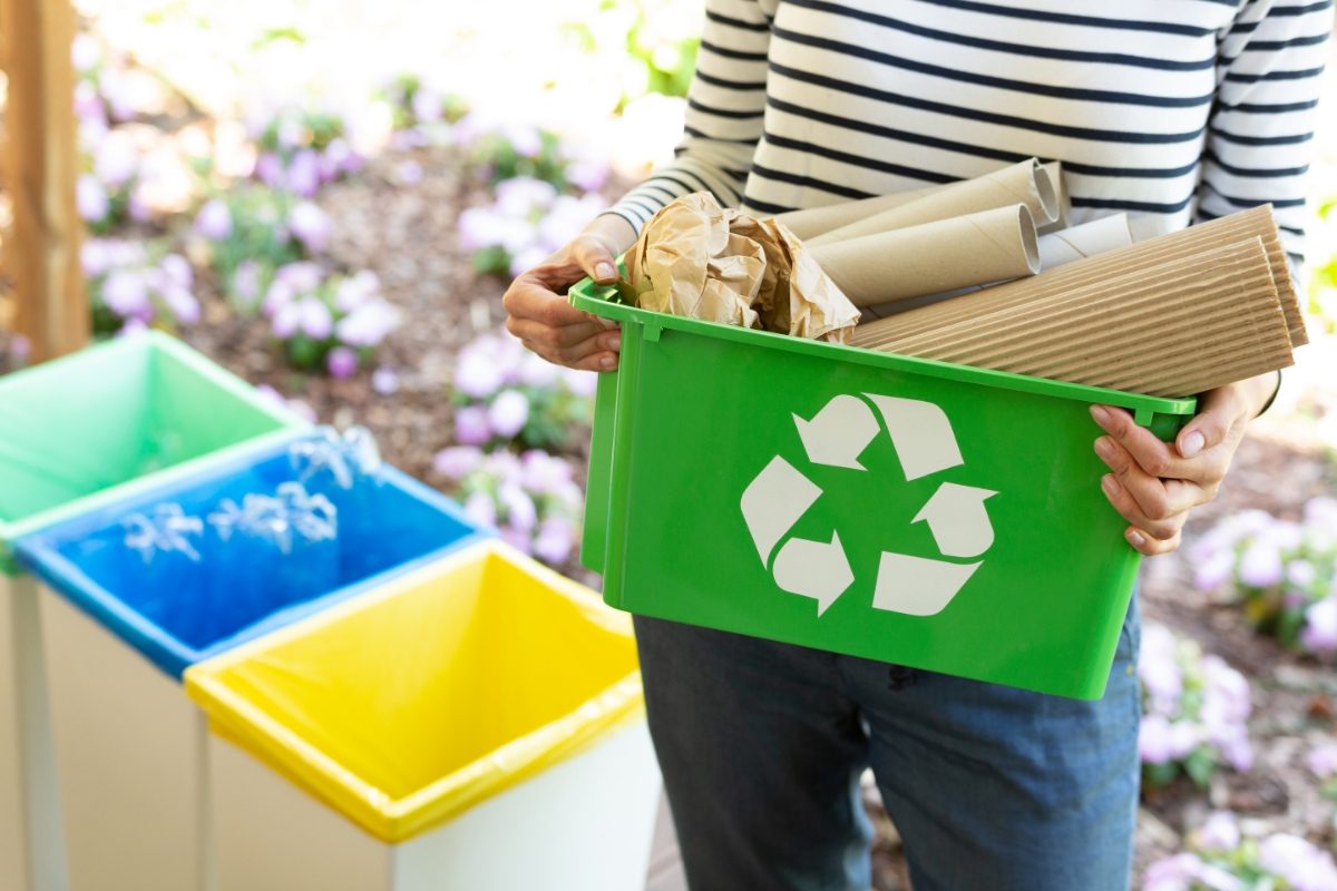 Woman a green basket with recycle sign filled with papers