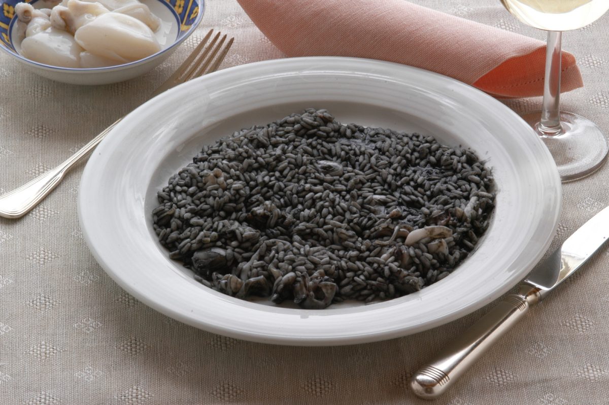 Close-up of Risotto al Nero di Seppia served in a white plate with dining utensils