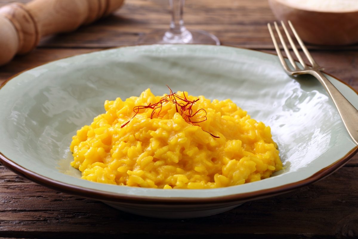 Risotto alla Milanese dish made with medium grain rice, broth, saffron, and cheese served on a white plate