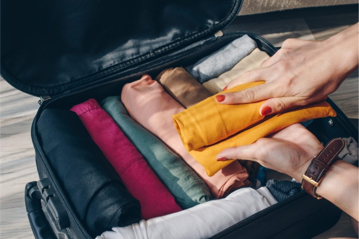 Woman packing clothes by arranging and putting on an open suitcase