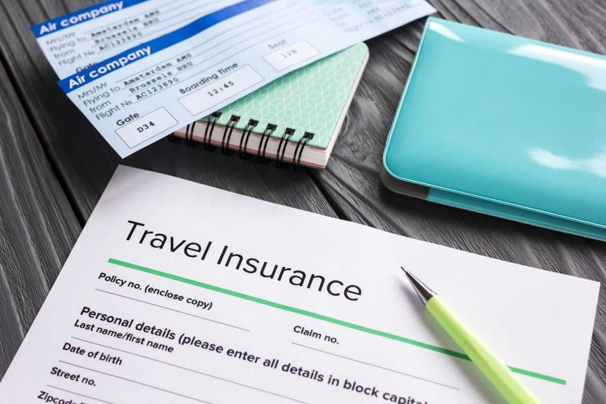 Close-up of a blank travel insurance form next to plane tickets, pen, and passport