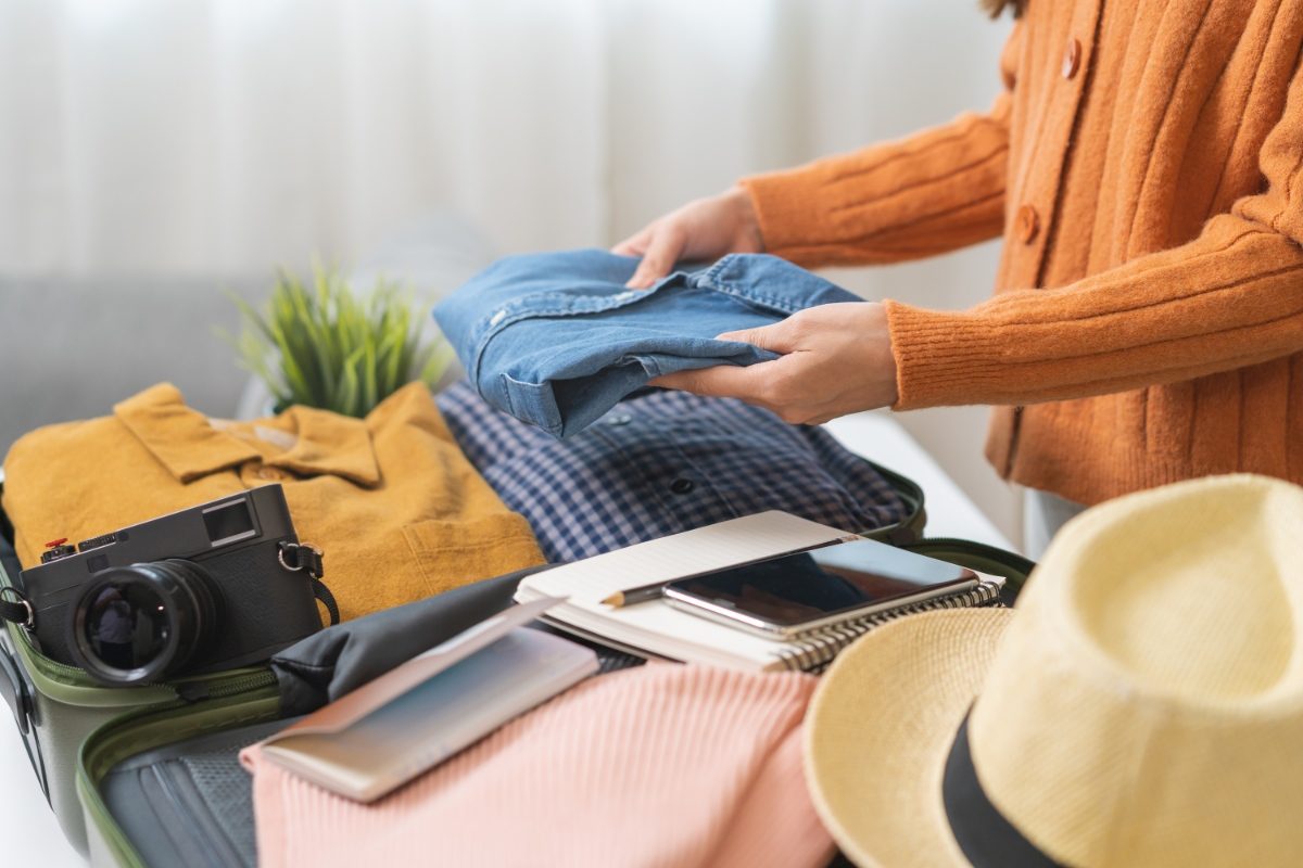 Woman packing clothes and travel essentials on a suitcase for travel