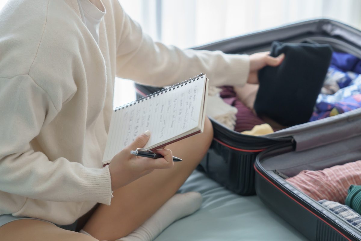 Woman packing for travel and holding a travel packing checklist