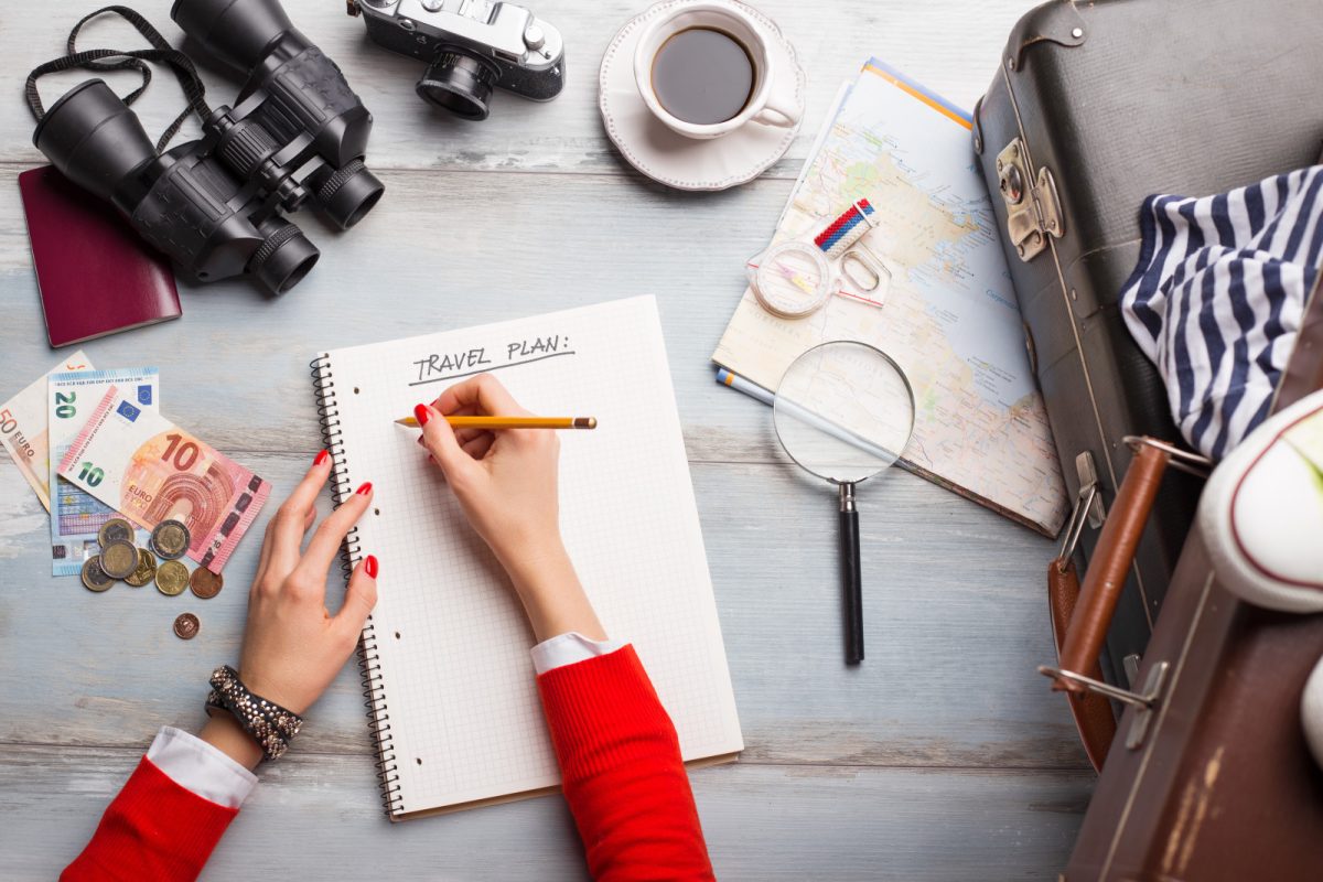 Woman making a travel plan on a huge notebook surrounded with travel essentials