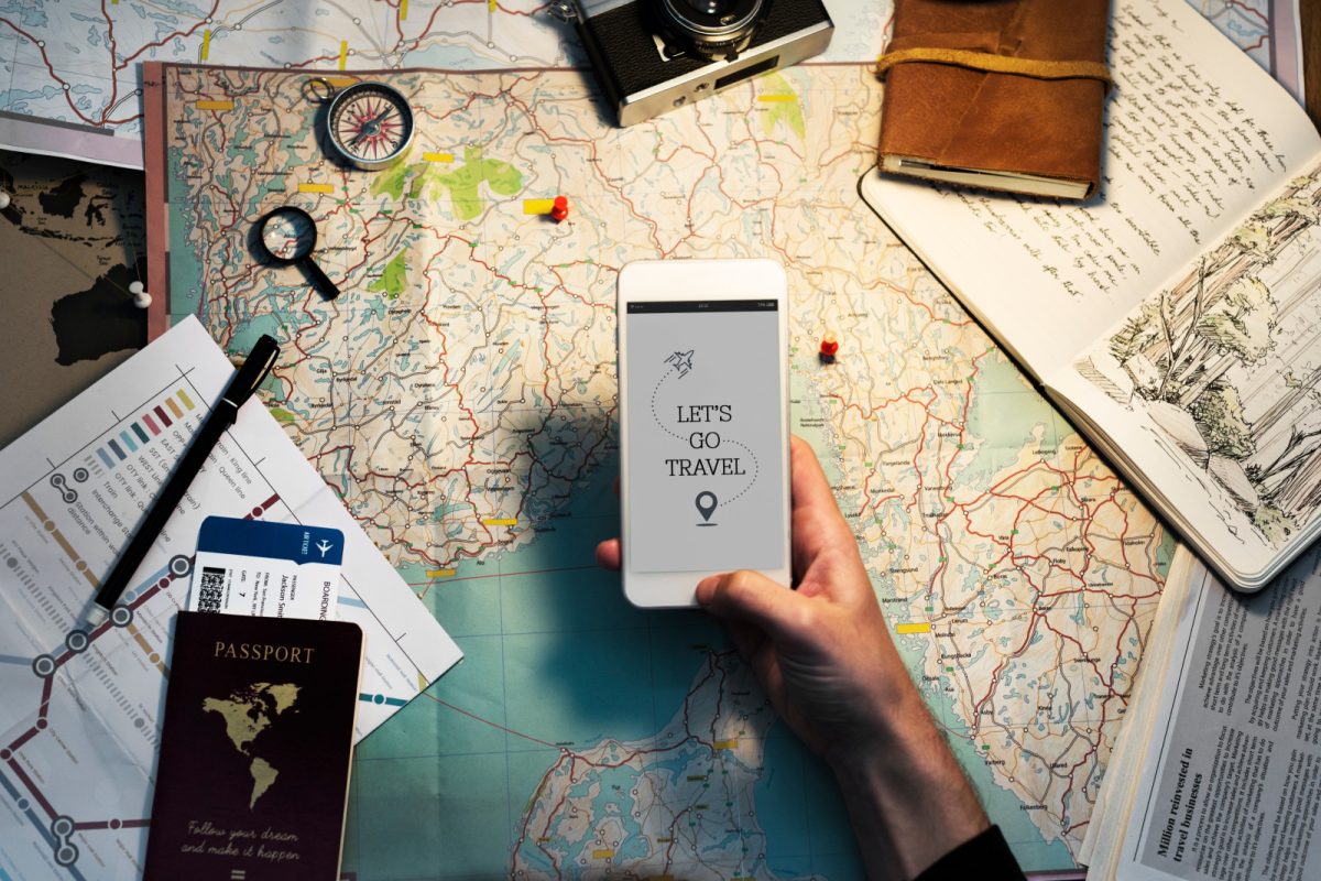 Hand holding a phone with map, journal, and travel itinerary in the background