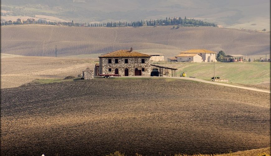 A stunning Tuscan farmhouse surrounded by lush greenery and vibrant flowers, nestled in the picturesque countryside under a clear blue sky.