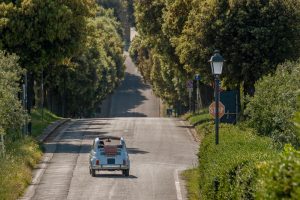 Old light blue Fiat 500 convertible car driving on a road in Tuscany, Italy