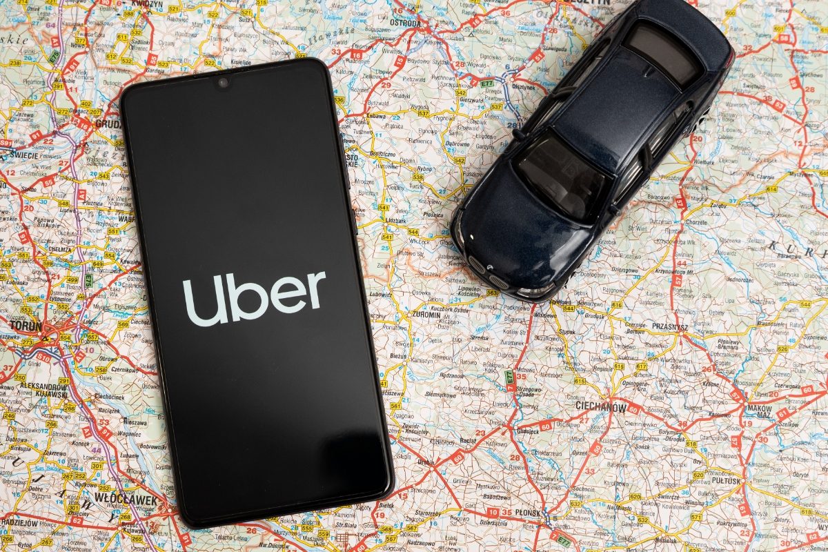 Phone displaying the Uber ride-sharing app logo sits next to a toy car placed on top of a map