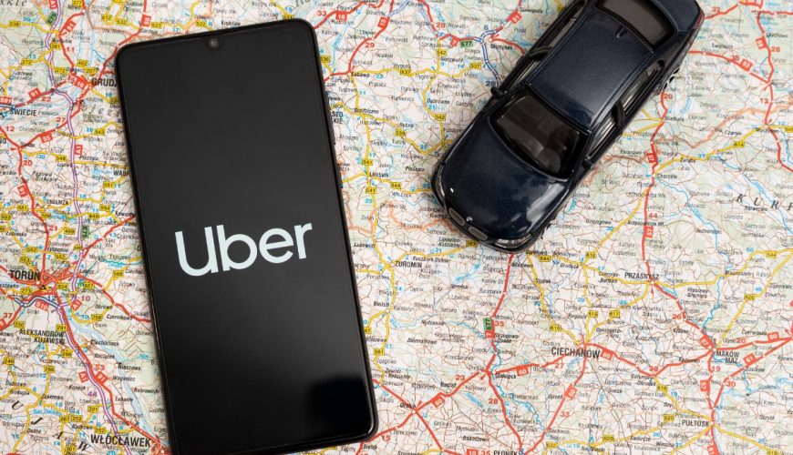 Phone displaying the Uber ride-sharing app logo sits next to a toy car placed on top of a map