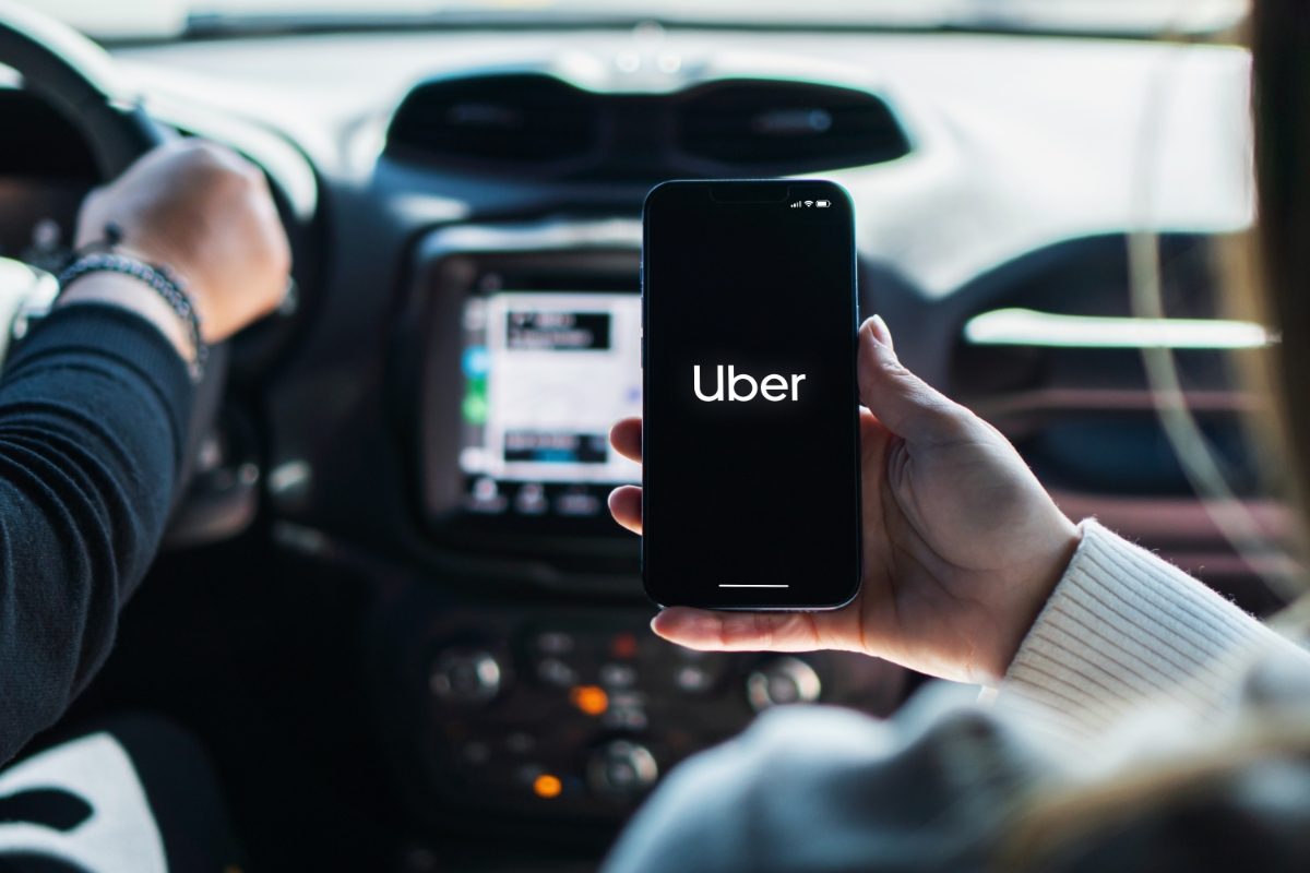 Girl sitting inside a car holding a smartphone displaying the Uber app