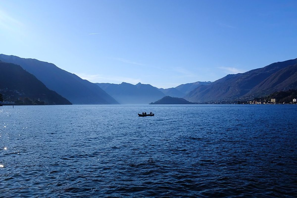 A serene view of Lake Como, Italy, under a clear blue sky, with lush greenery surrounding the tranquil waters.