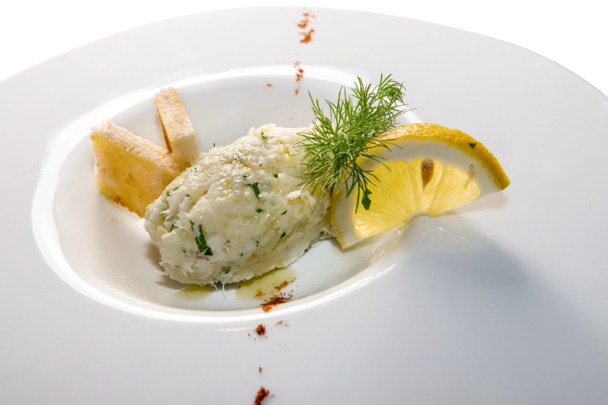 Close-up of a baccalà mantecato Venetian appetizer served on a whote plate with lemon slice and toasted bread