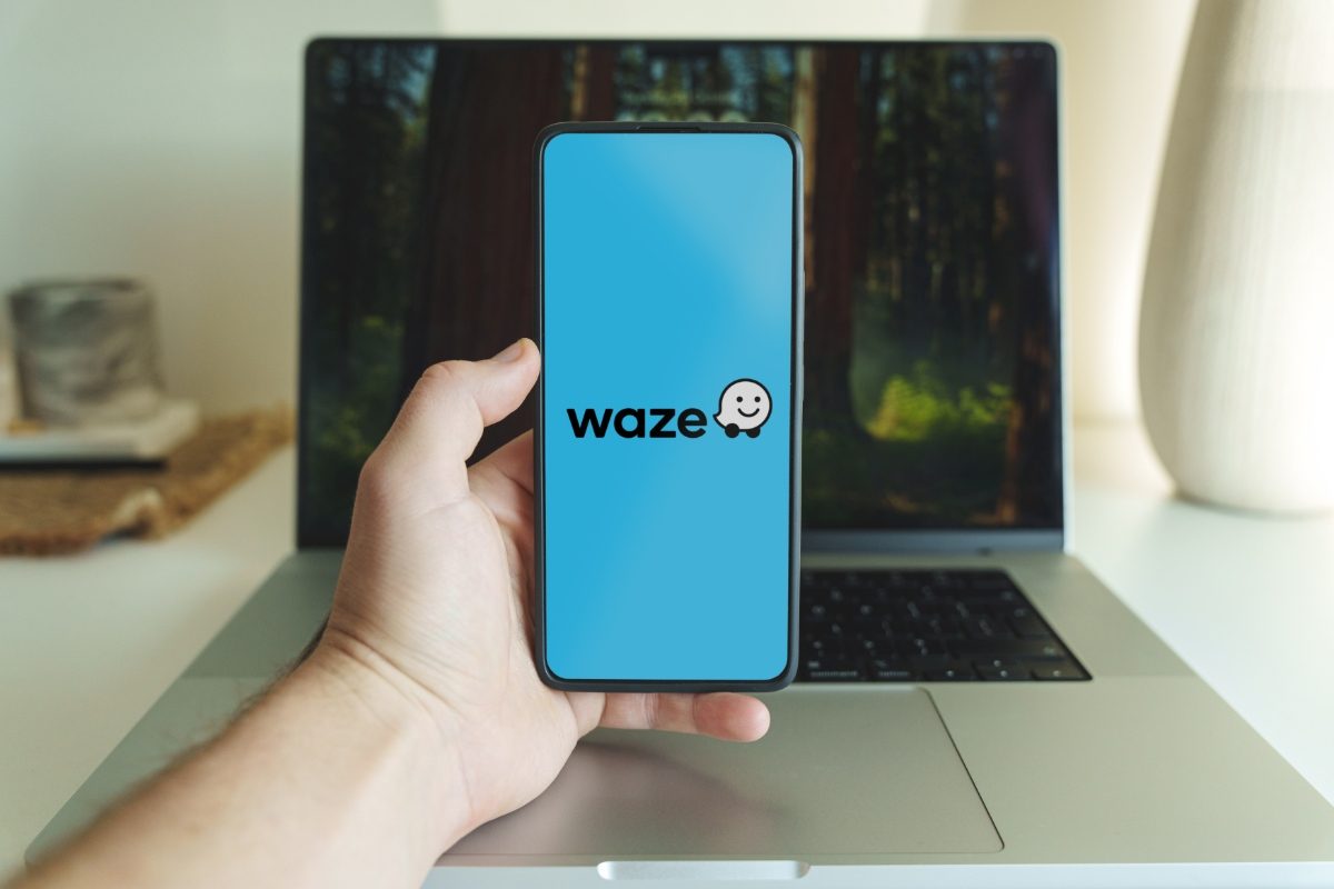 Hand holding a phone with the Waze navigation map application logo shown on the screen