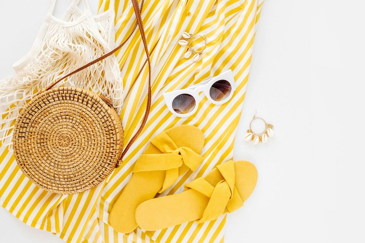 Top view of a yellow summer dress, sunglasses, and coordinating accessories